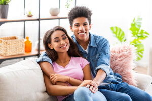 Happy teen lovers having rest at home, embracing on couch