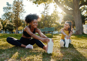 Female diverse friends doing stretching exercise in the park - diverse friends warming up before doing group exercise
