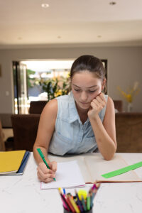 Caucasian teenager girl sitting at table and doing homework